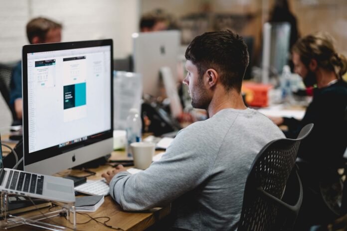 license-management-tools-featured man in gray sweatshirt sitting on chair in front of iMac