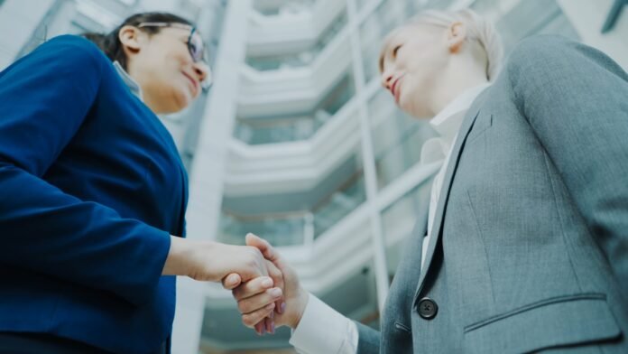 how-ai-improves-change-management-featured Two businesswomen shaking hands in a modern office building.